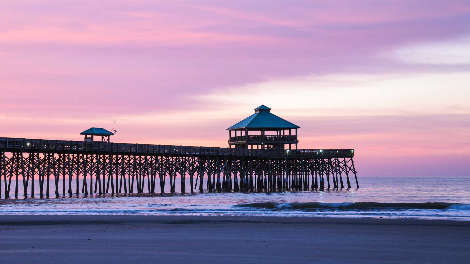 The iconic Folly Beach Pier stretching into the Atlantic Ocean during a purple-hued sunset.